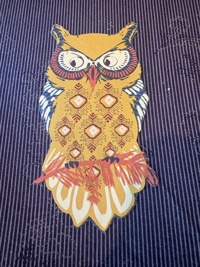 An owl fabric cut out on a piece of purple fabric.