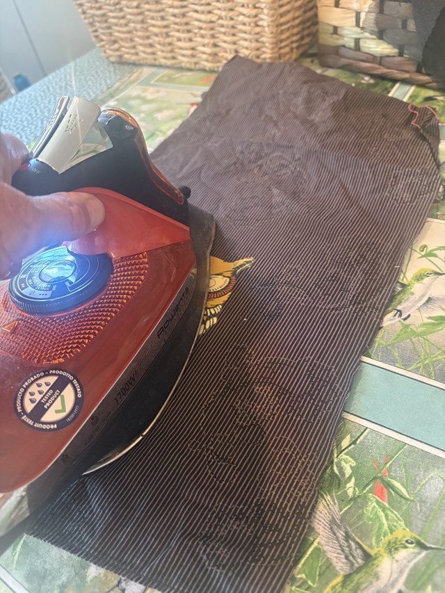 A person with a red iron ironing two pieces of fabric together on an ironing board.