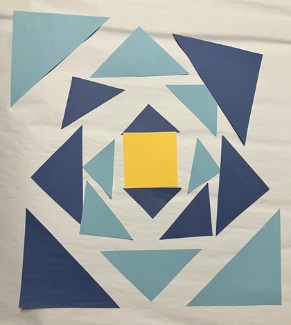 A series of blue paper triangles laid out in a square shape. A yellow square in the middle.