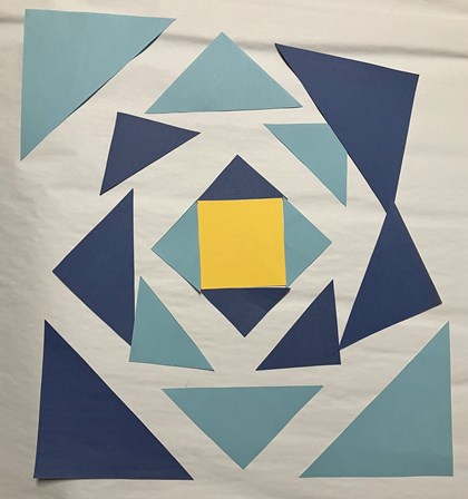 A series of blue paper triangles laid out in a square shape. A yellow square in the middle.