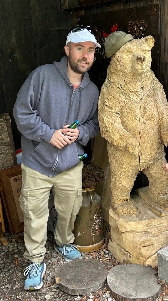 A man stands beside a carved bear statue.