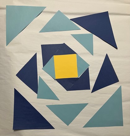 A series of blue paper triangles laid out in a square shape. A yellow square in the middle.