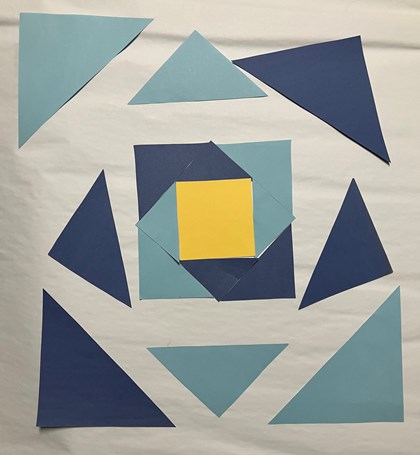 A series of blue paper triangles laid out in a square shape. A yellow square in the middle.