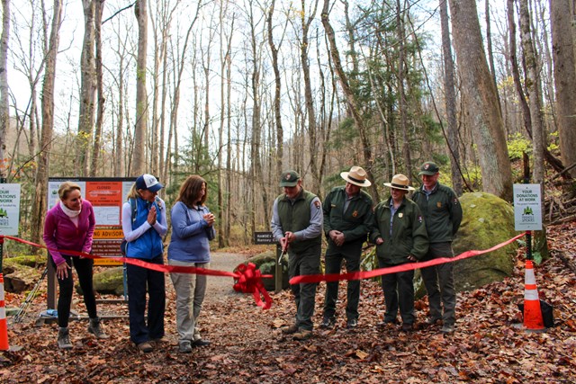 A ribbon being cut at a trailhead by a ranger, a few others stand by and watch.
