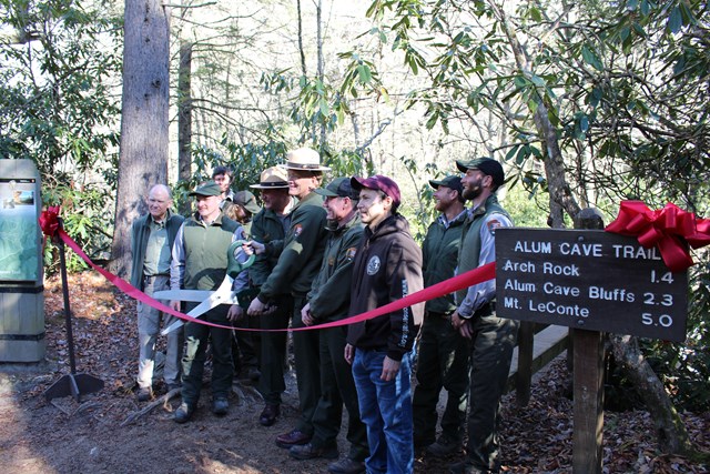 A group of rangers cutting a ribbon at alum cave trailhead.