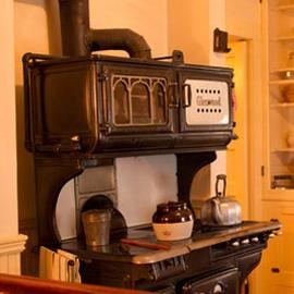 Kitchen in historic house with gas and coal stove at center.