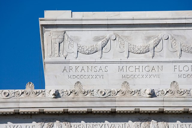 A corner of the Lincoln Memorial depicts the names of states with roman numerals and a sculpture above that appears as bunting.