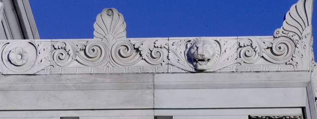 The top edge of a marble building depicts oak leaves, spirals, and a lion's face.