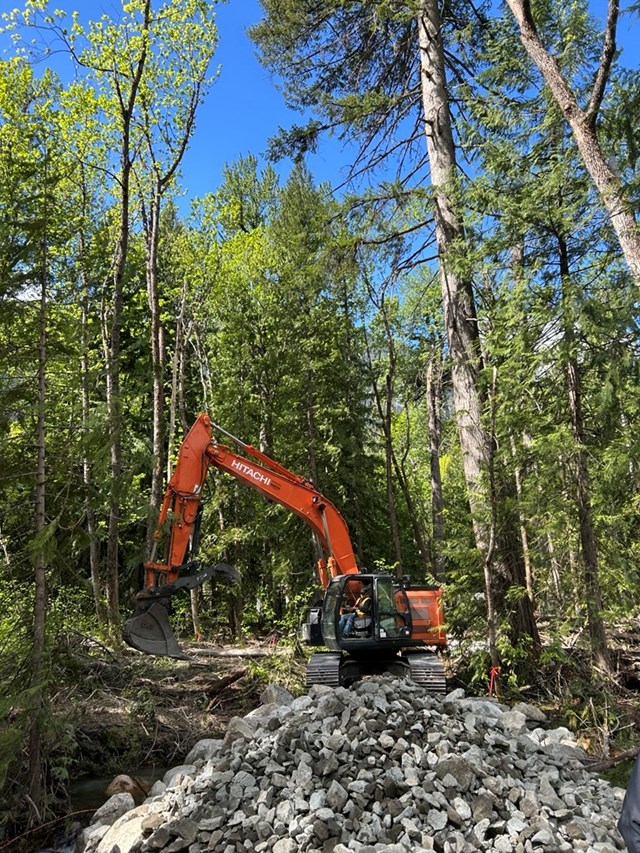 An excavator behind a large pile of gray rocks in a forest