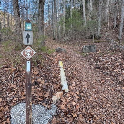 A trailhead leads out from the foreground, marked by a signpost to the left. 