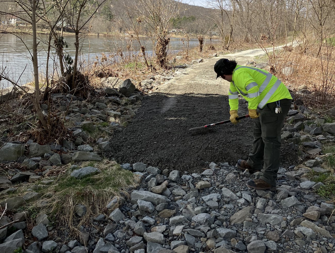 staffperson rakes gravel to level trail along the river