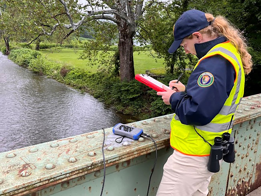 Young woman writes something on clipboard. Next to her is a small machine with a screen.