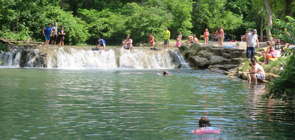 water flowing over a ledge with people swimming in the water above and below