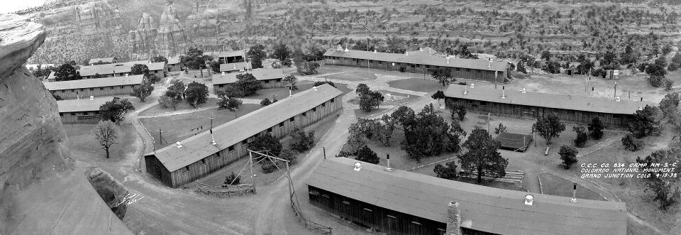 black and white photo of several long, wooden barracks-style buildings with a central courtyard, canyon cliffs in the background