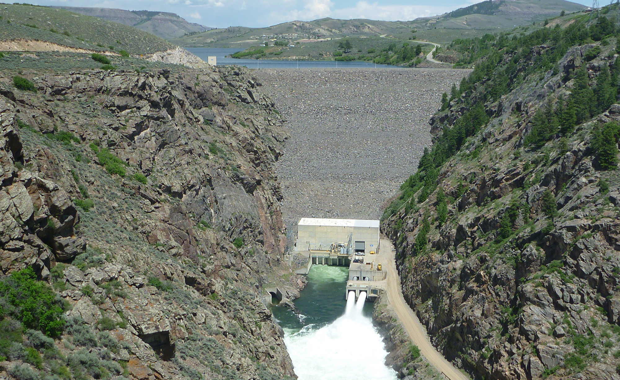 Historic black and white image of an earthen dam construction between two canyon walls.
