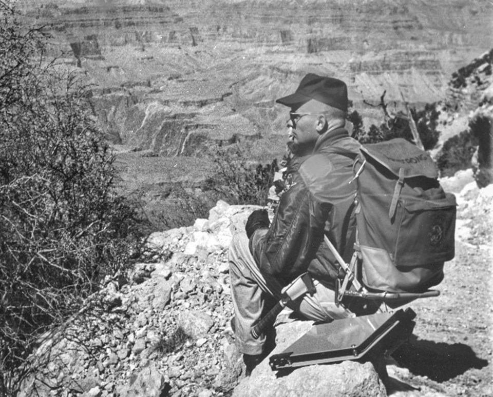 Man with backpack sitting on rock on trail looking down into canyon