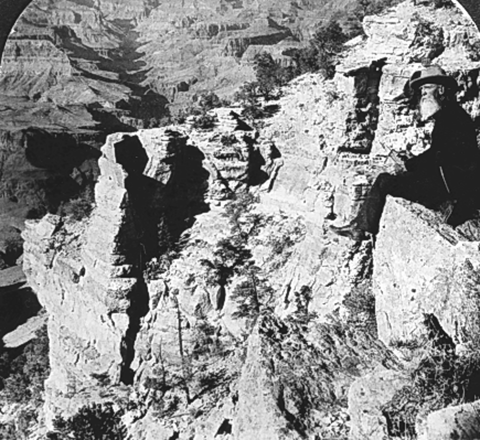 Man sitting on cliff edge with canyon in background