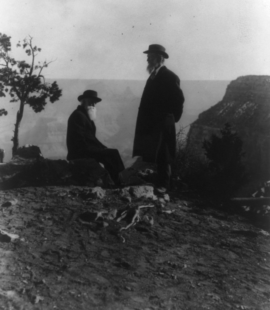 Two men stand on cliff edge with canyon in background