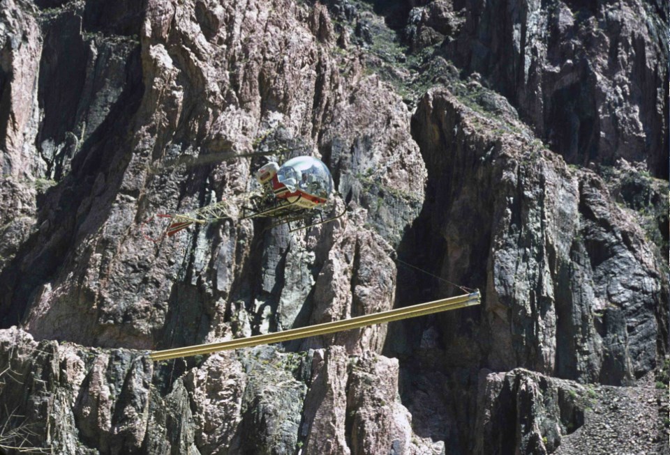 Helicopter carrying large pipe with cliff in background