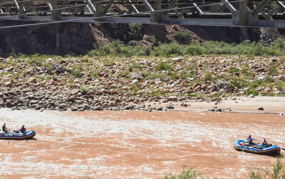 Women in a large wooden box above a river with cliffs in background