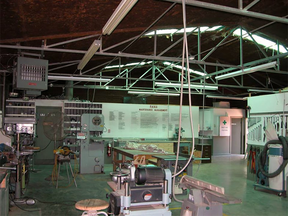 Tools and heavy machinery fill a metal room with concrete floors.