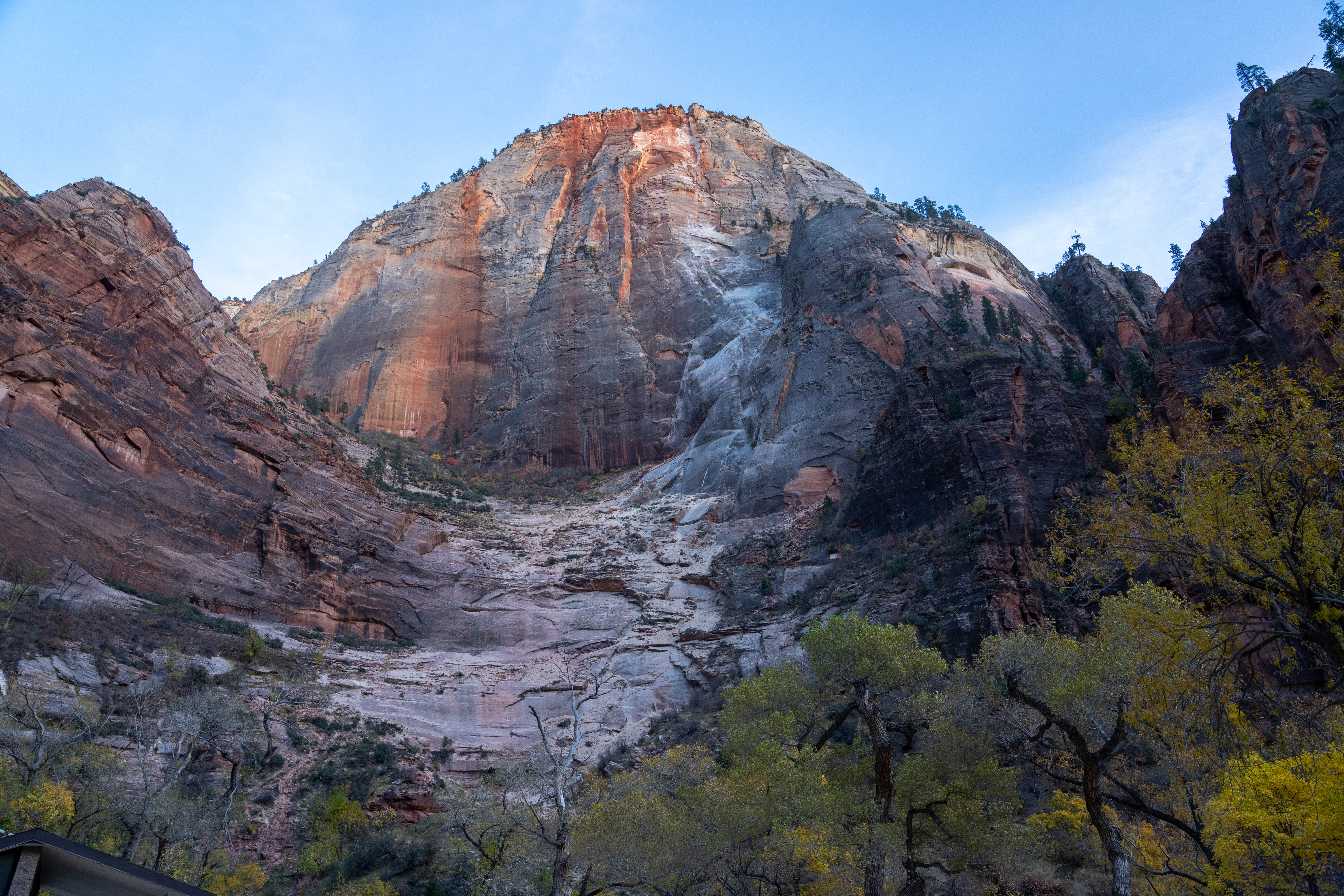 A large red orange and white sandstone peak with green foliage in the foreground