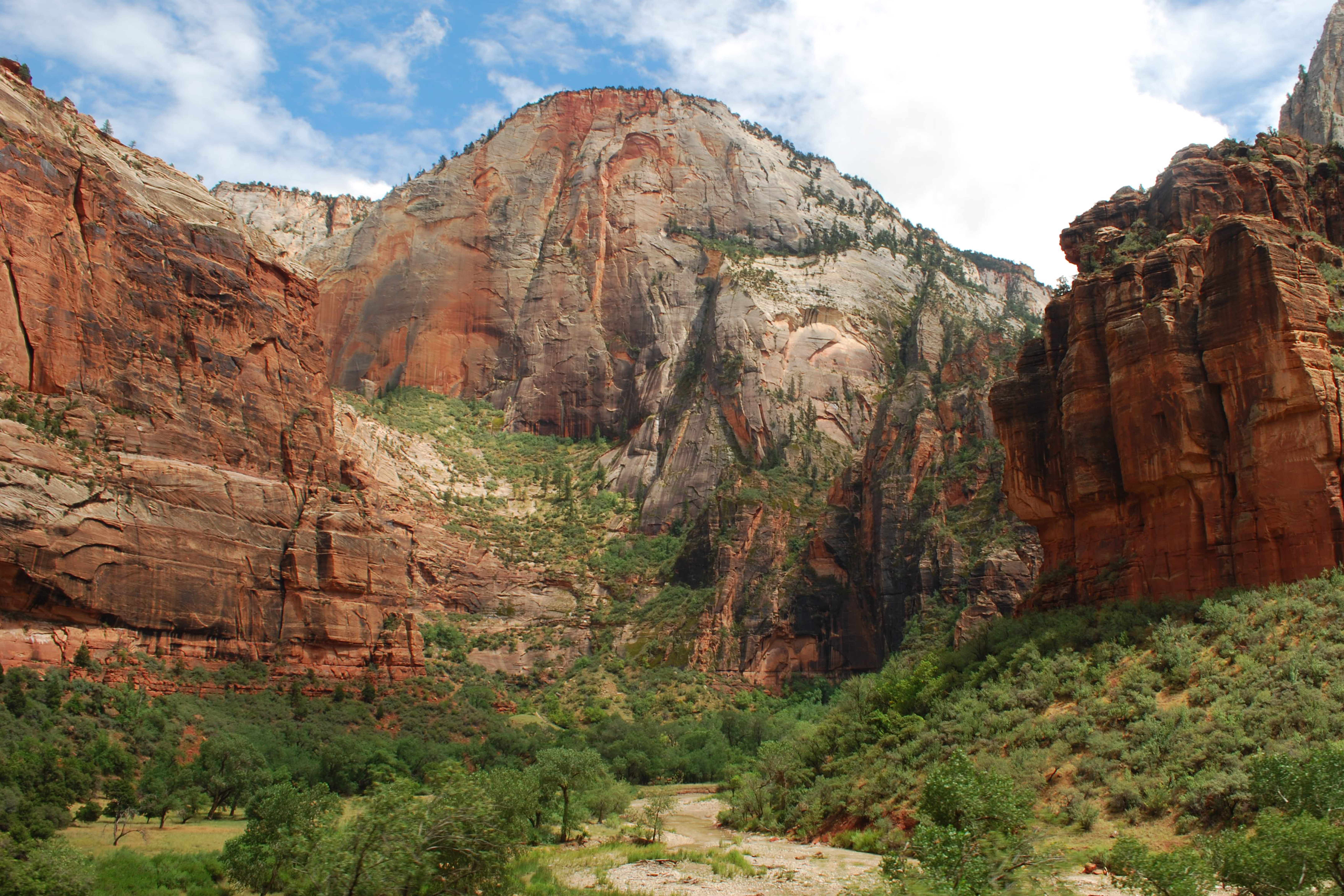 A large red orange and white sandstone peak with green foliage in the foreground