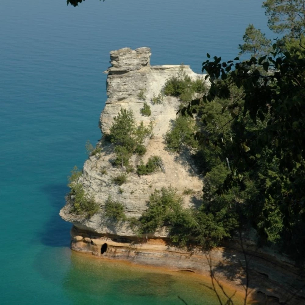 A sandstone rock formation with trees coming out of Lake Superior. The formation has two large formations on top (turrets).