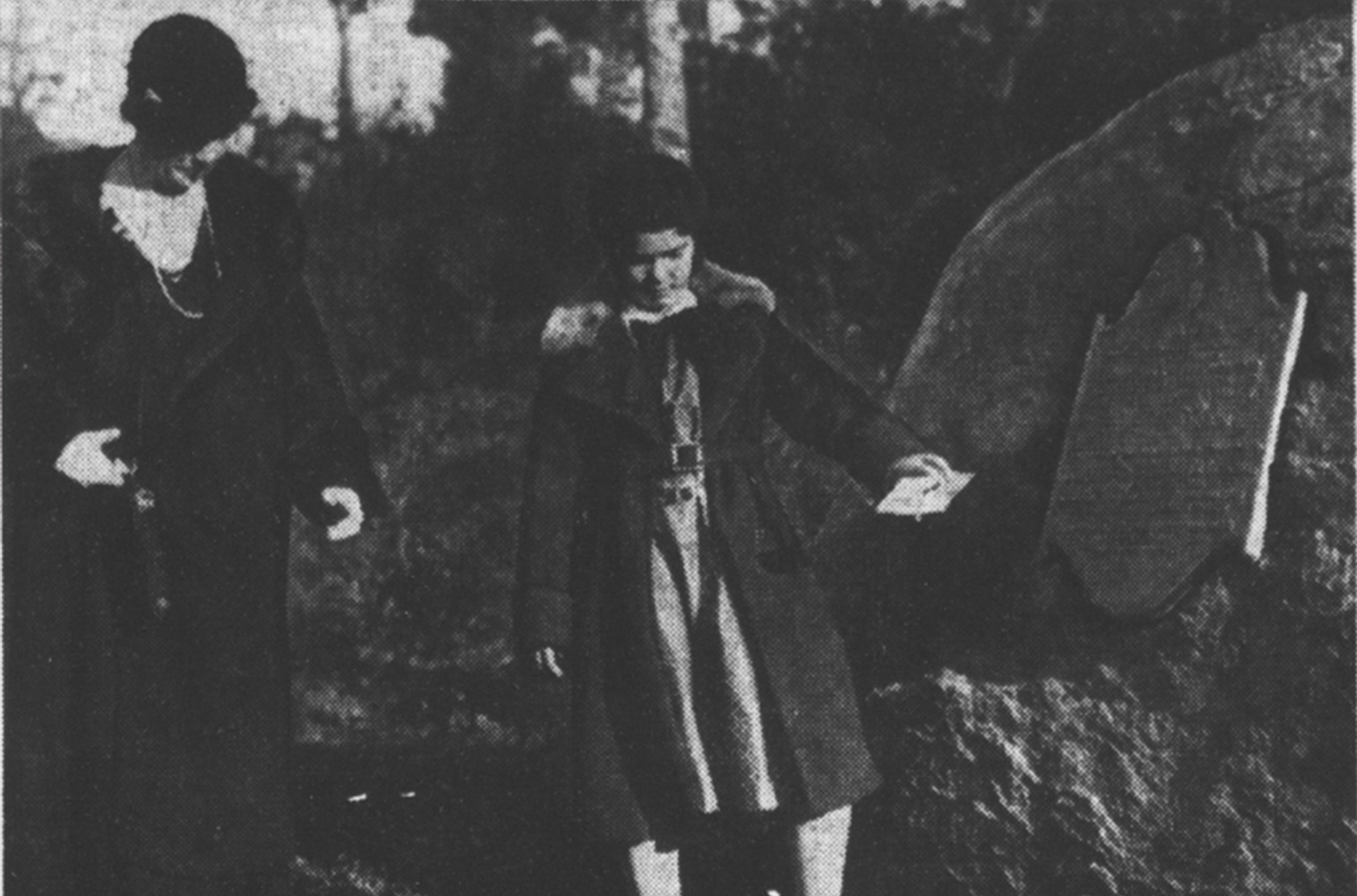 A black and white photo of a child sprinkling dirt in front of a boulder with a plaque