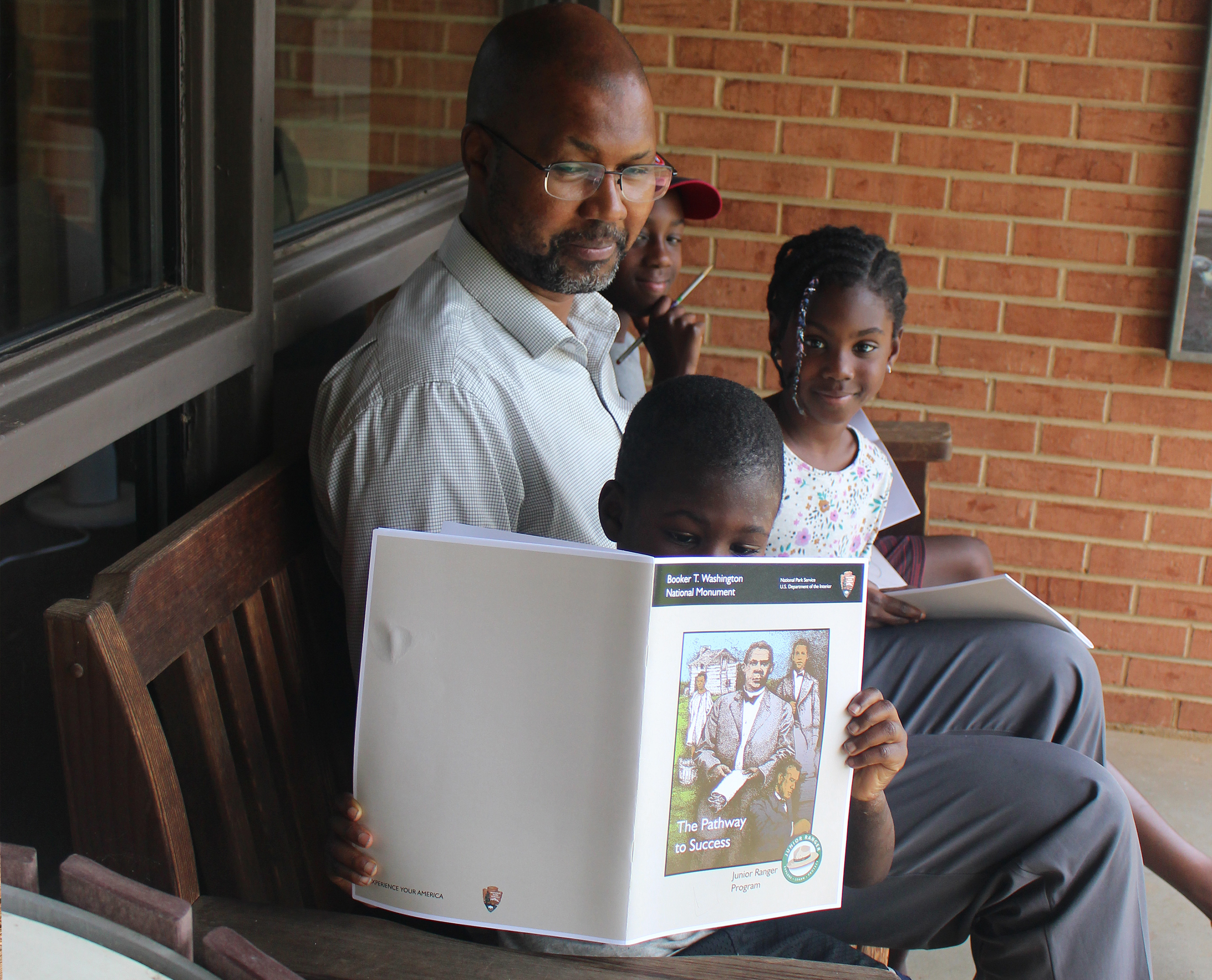 Three children and one adult stand in front of an interpretive wayside depicting slavery.