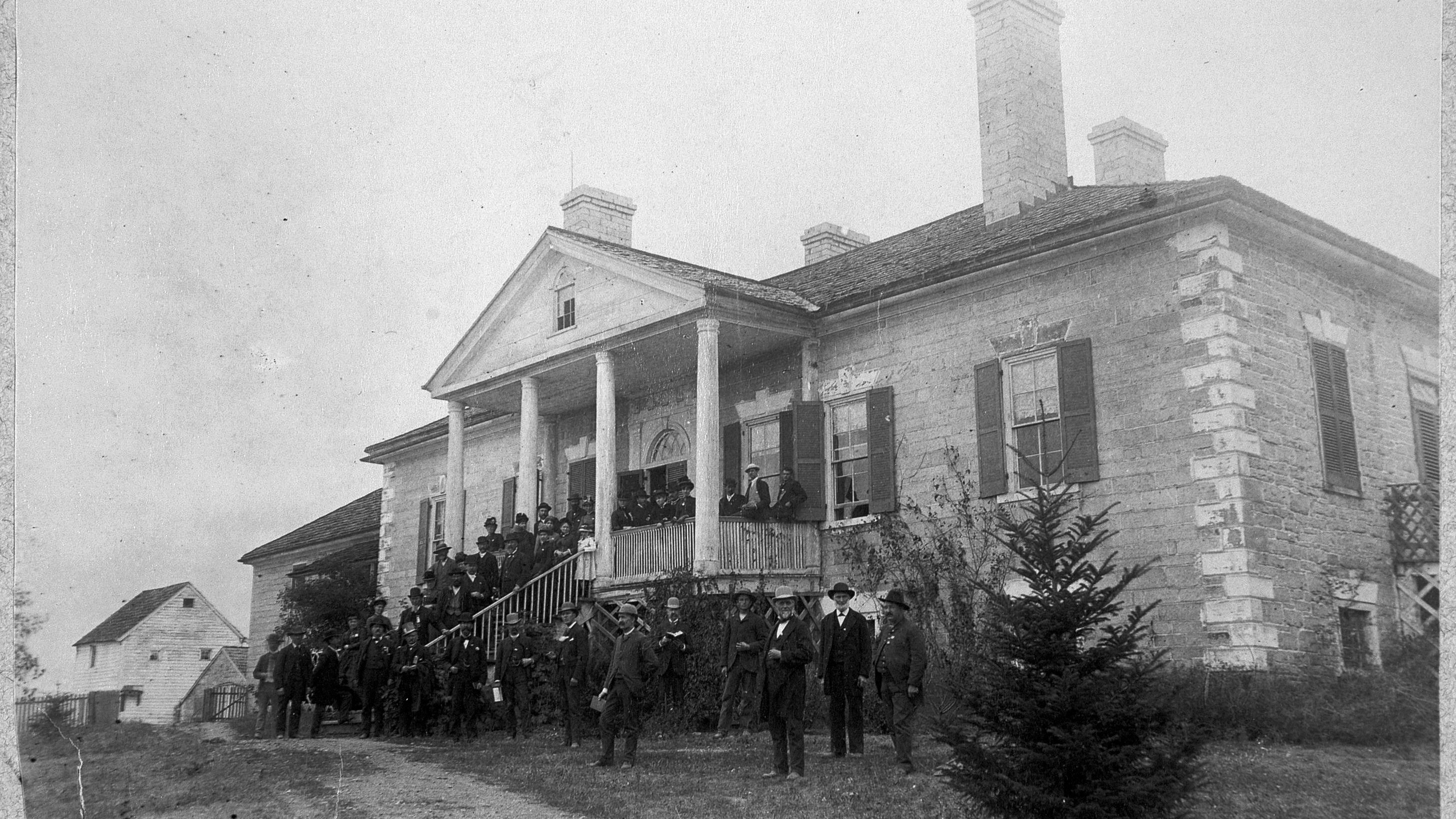 Large limestone plantation house, exterior stairs leading up to a columned front porch.