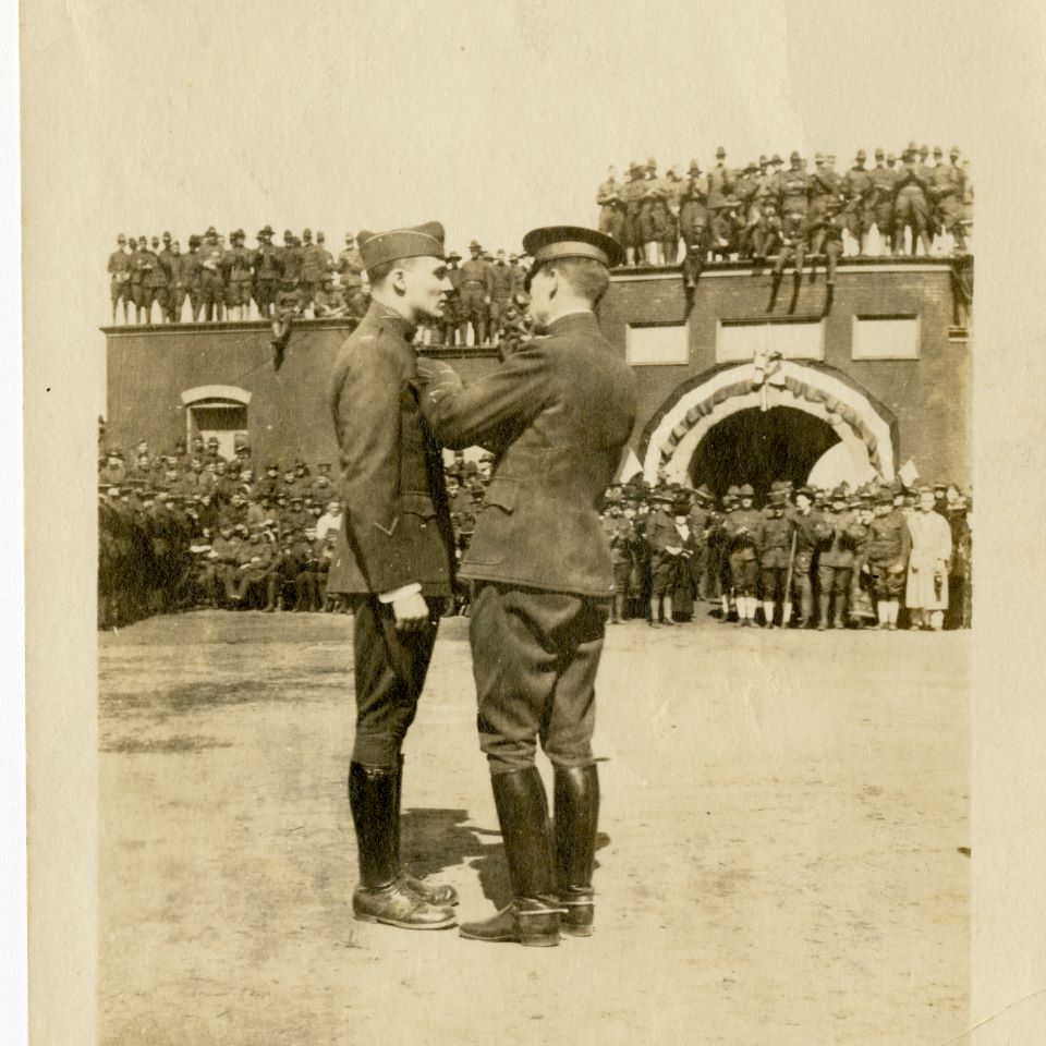 In front of a large crowd of soldiers, one presents to the other what appears to be a medal on the parade ground inside the Starfort.