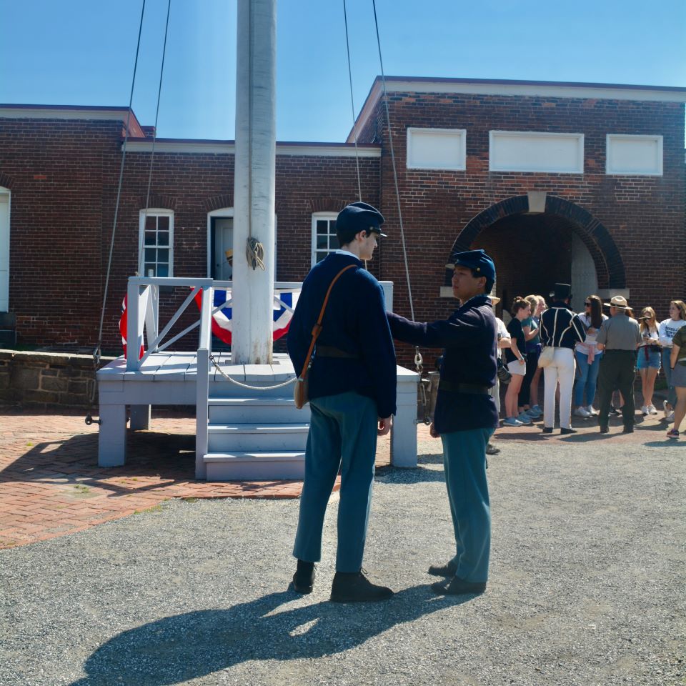 In front of a large crowd of soldiers, one presents to the other what appears to be a medal on the parade ground inside the Starfort.