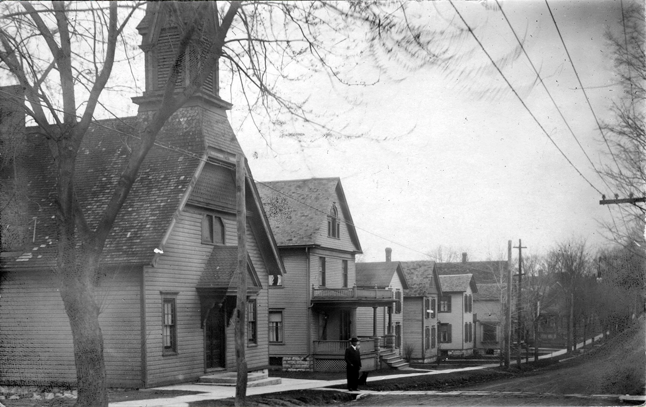A black and white photograph of a church and row of houses, looking up a street.