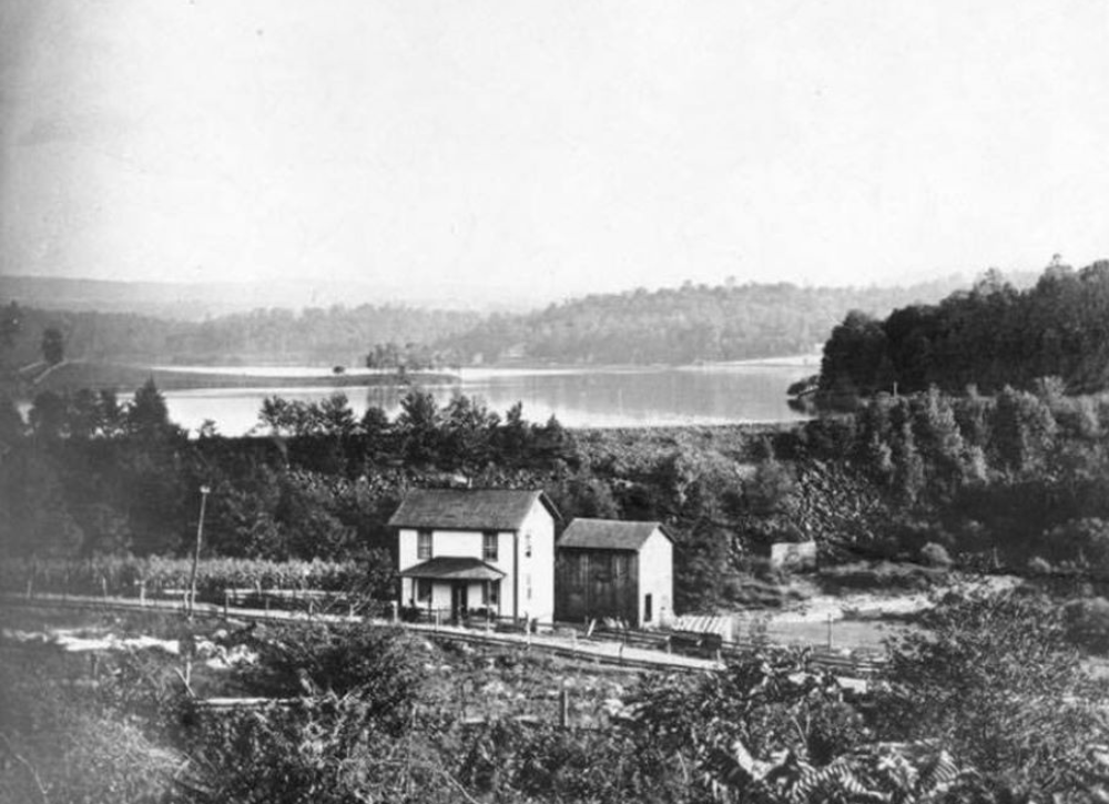 Lake held back by an earthen dam with a house below.