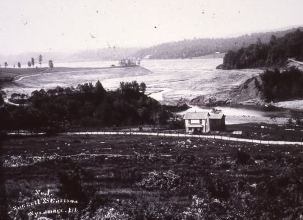 Lake held back by an earthen dam with a house below.
