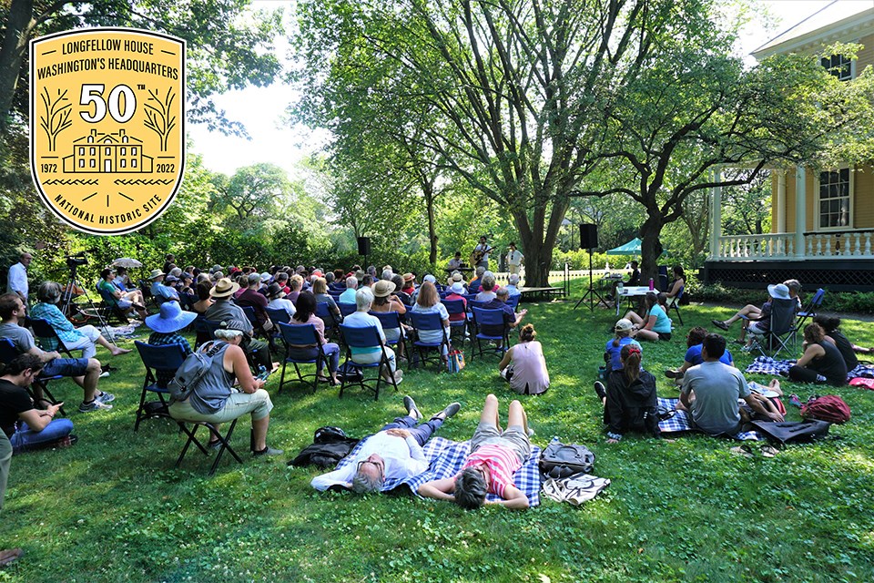 crowd seated on chairs and blankets on lawn to watch concert, with 50th anniversary logo