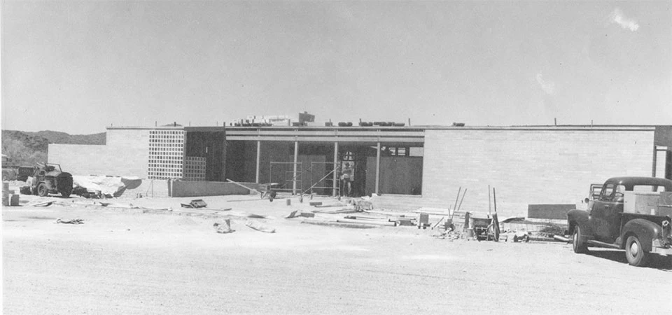 Construction materials surround the entrance of a long, single-story structure.