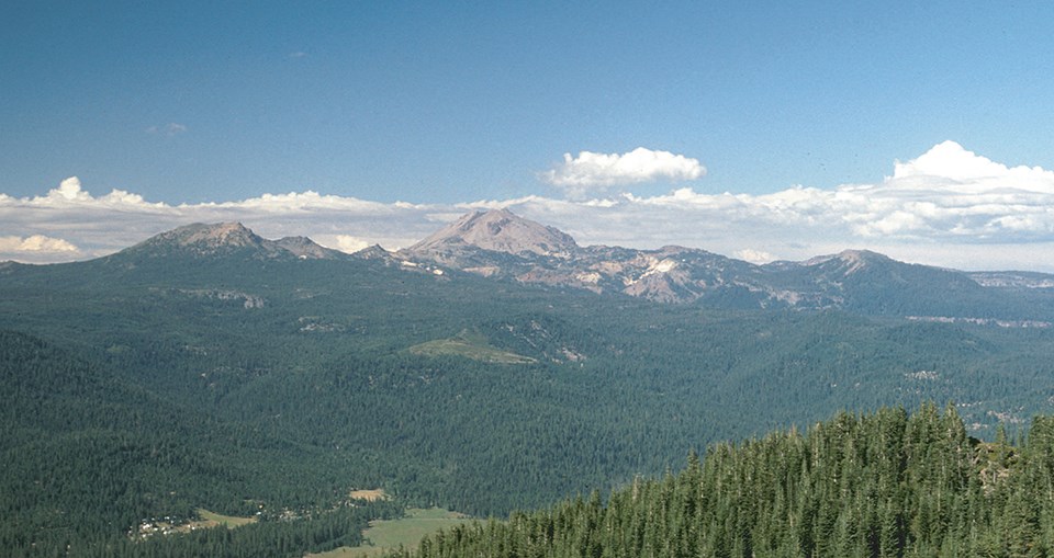 forested landscape with volcanic peaks in the distance.