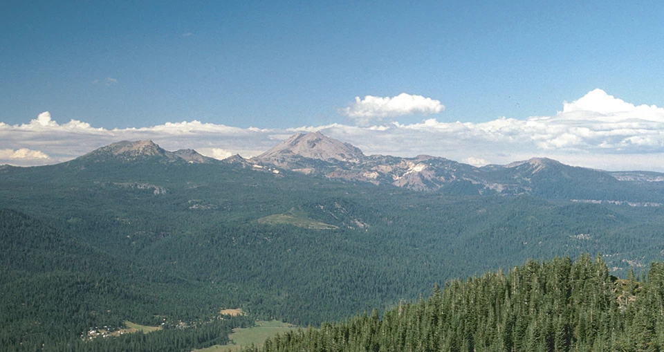 forested landscape with volcanic peaks in the distance.