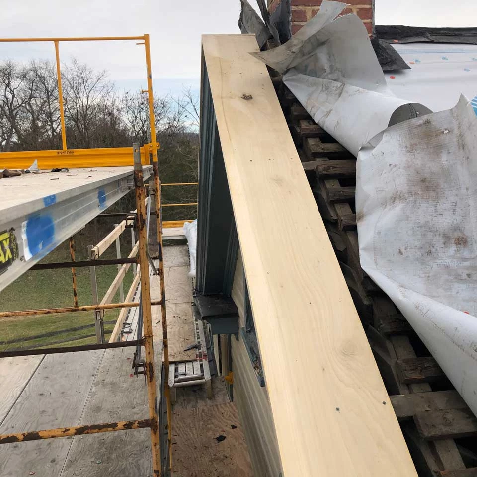 Peak of the end of the roof exposed. The large gable board is dark brown and has a number of places where holes exist and wood is rotten.