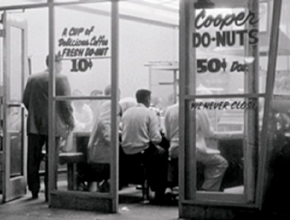 Photo of glass walled cafe that advertises donuts.