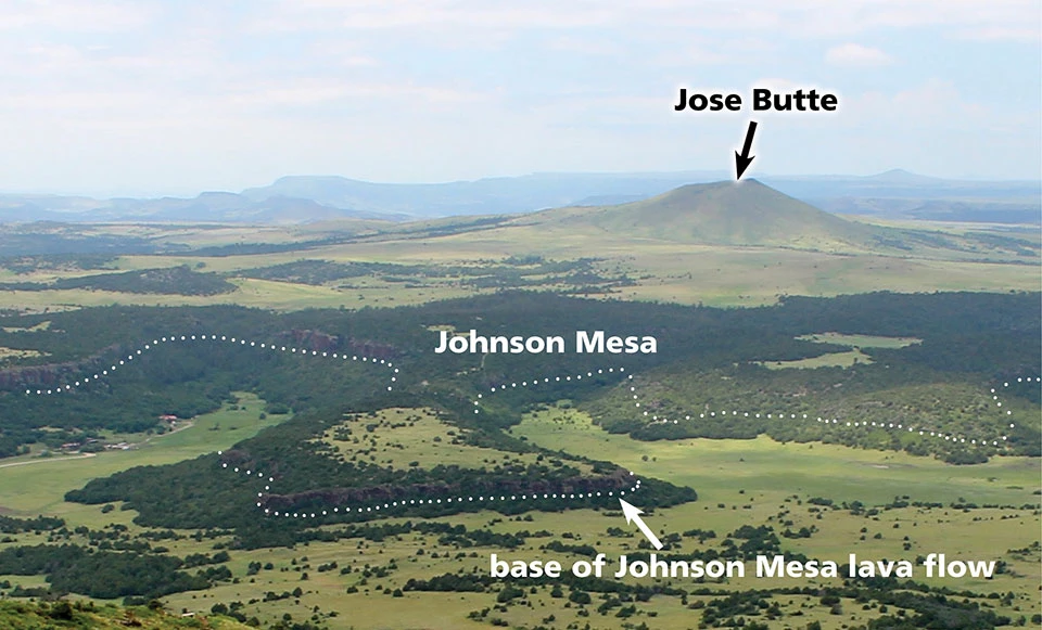 photo of a volcanic landscape with a large mesa and a cinder cone all covered with grasses and trees