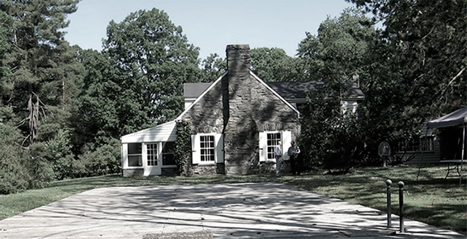 Wood covers a rectangular pool, surrounded by turf and trees beside a stone cottage