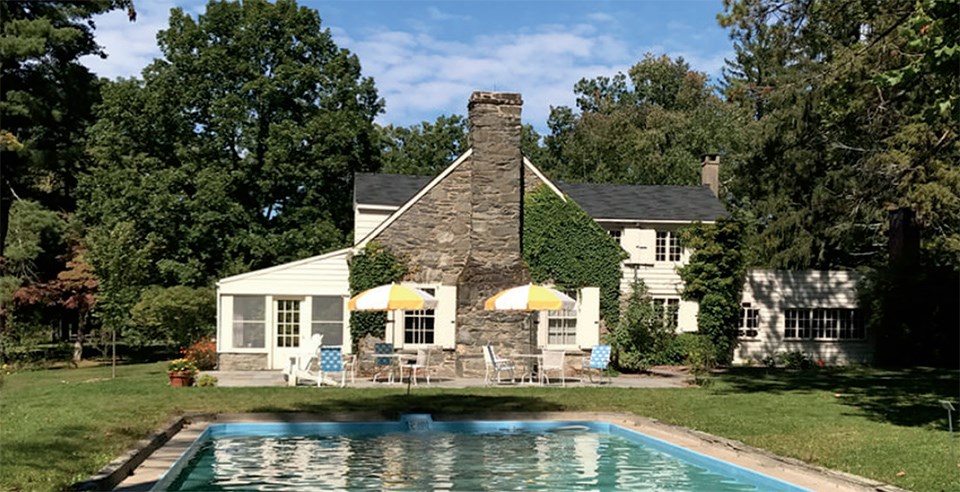 Wood covers a rectangular pool, surrounded by turf and trees beside a stone cottage