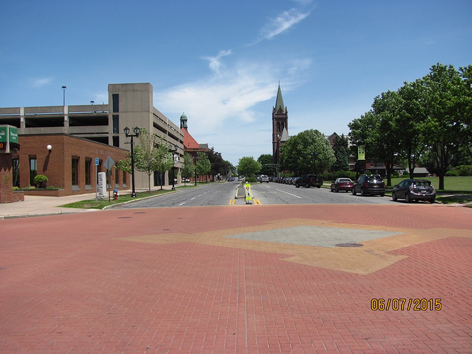 A city street covered in dirt with construction going on along the length. A church steeple in the distance.