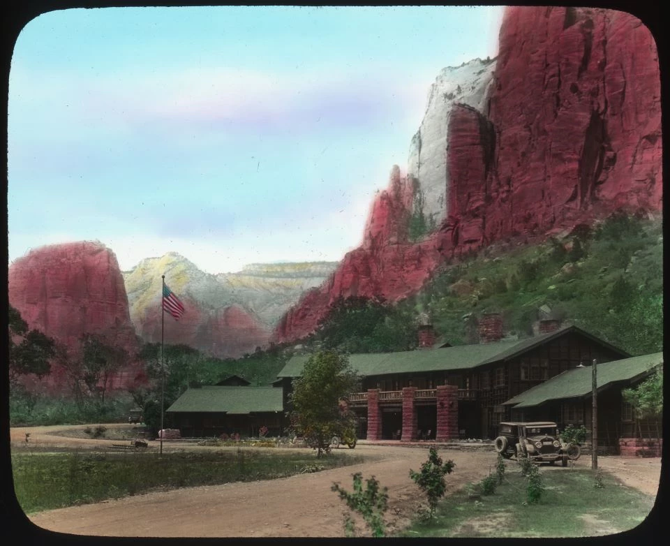 Black and white photo of a large wooden building with an old-fashioned car at the bottom of a cliff.