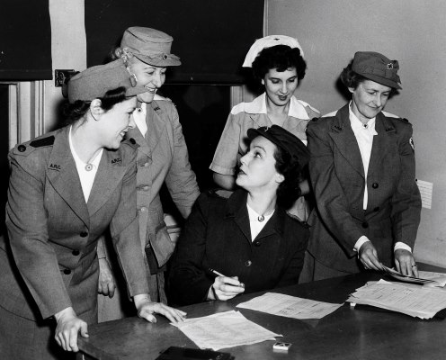 Black and white photo of five uniformed women working at a desk. Black and white photo of five uniformed women working at a desk.