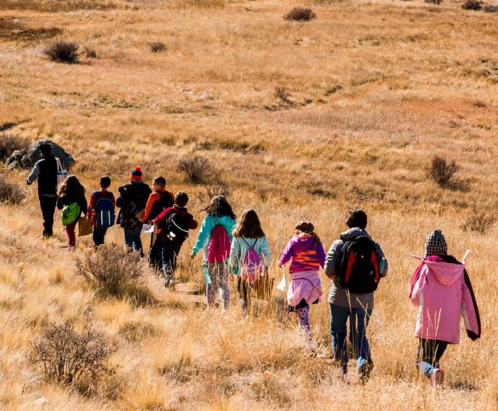 People dressed in jackets walking through a field of tan grass toward a brown wooden bridge. People dressed in jackets walking through a field of tan grass toward a brown wooden bridge.