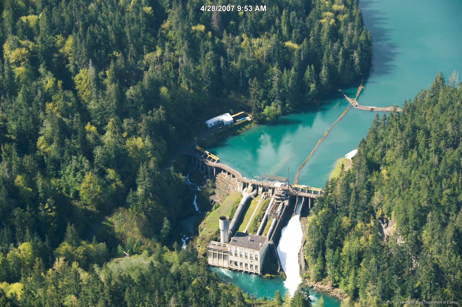 Aerial view of dam structure in river valley surrounded by trees Aerial view of dam structure in river valley surrounded by trees